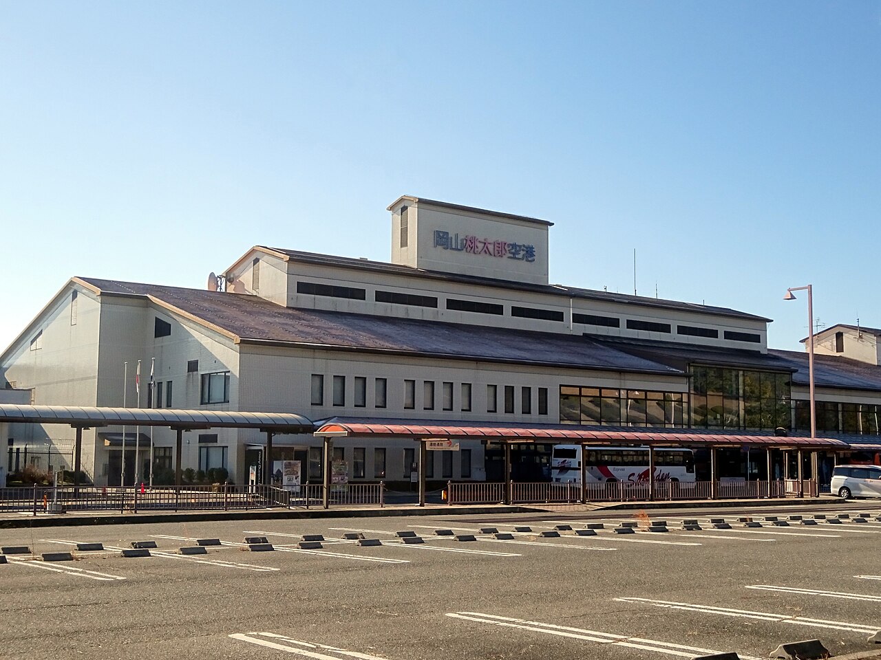 Okayama Momotaro Airport terminal sign and red curbside canopy beyond a parking area