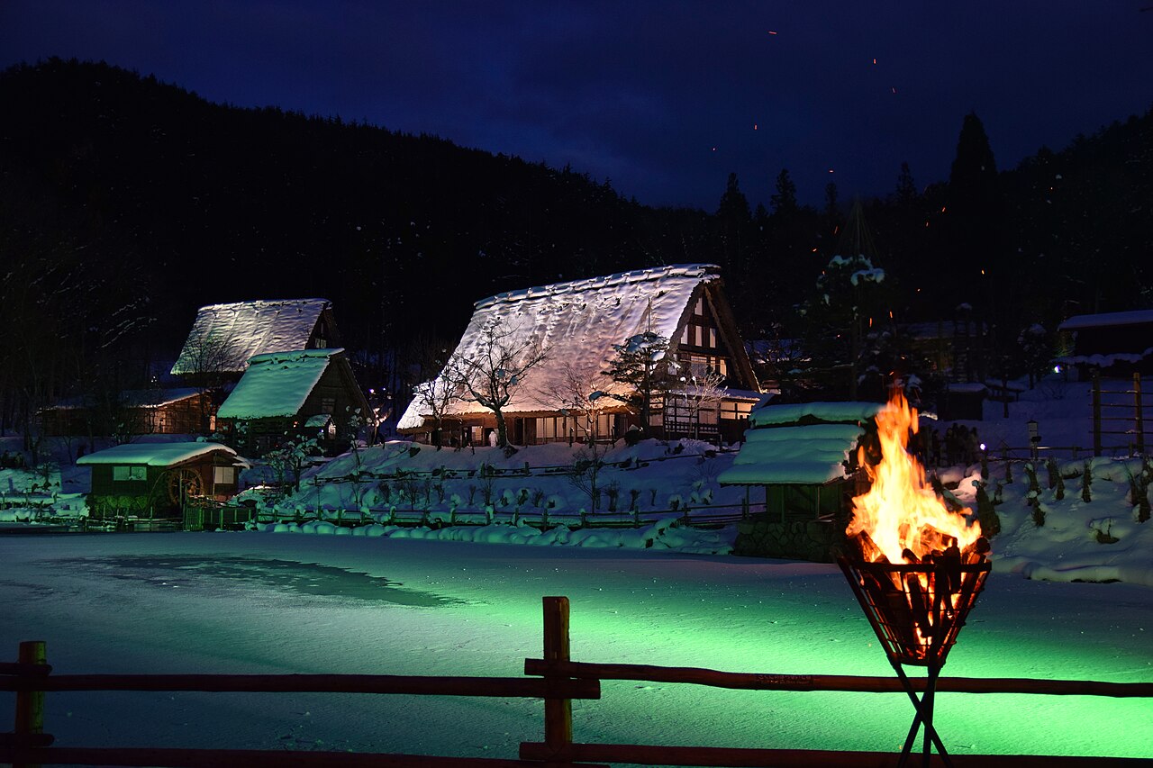 Snow-covered traditional houses and an illuminated pond at Hida Folk Village