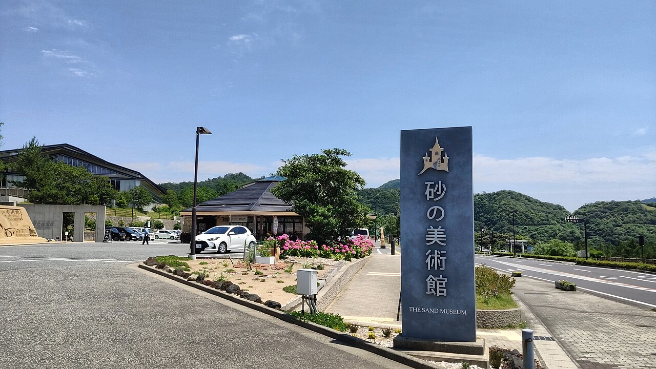 Vertical Sand Museum sign beside the road and exterior buildings in Tottori
