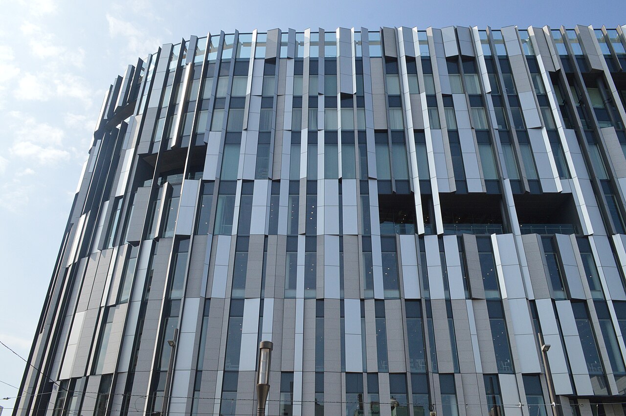 Curved TOYAMA KIRARI facade with vertical glass and metal panels against a blue sky