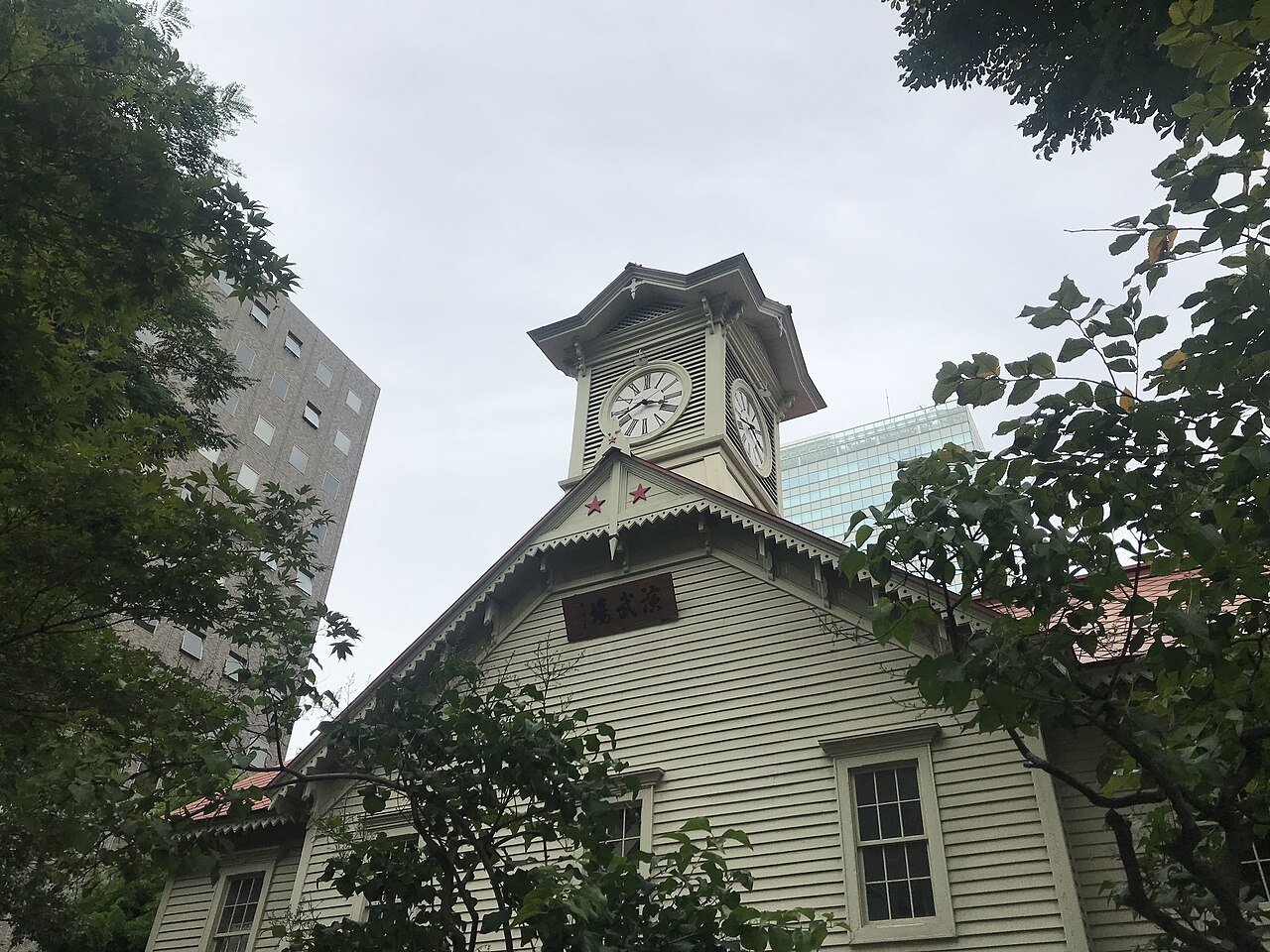 Sapporo Clock Tower with its clock and red star details between trees in 2022
