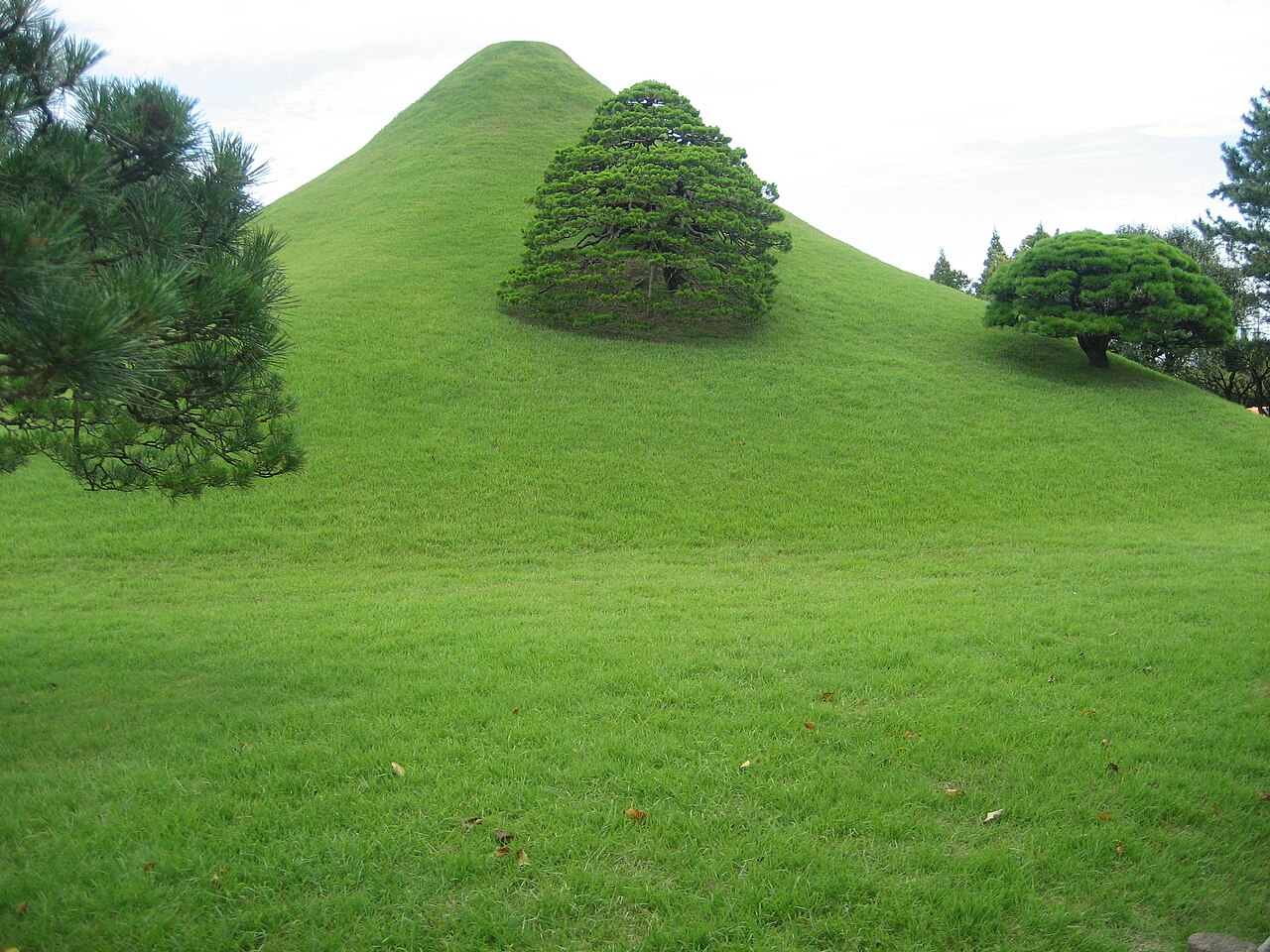 A green conical hill and pruned pine trees in Suizenji Jojuen garden