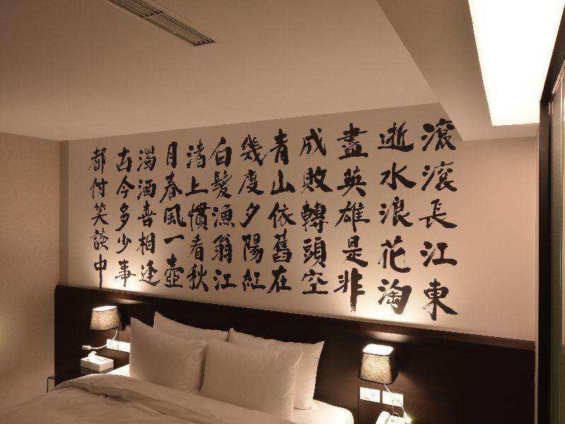 Travel Art Inn · 島宇居行藝文旅: A partial bedroom view with pillows, headboard lighting and calligraphy decoration