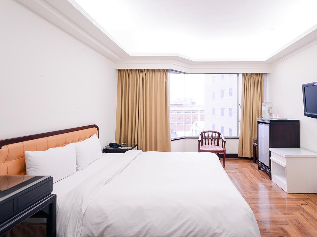Peach Hotel: A room showing a large bed, window, refrigerator and chair