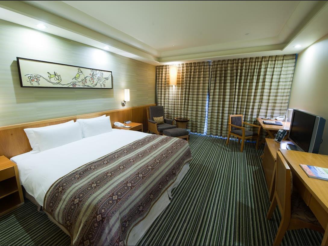 Nice Prince Hotel: A bedroom with a large bed, desk, television, armchair, round table and curtains