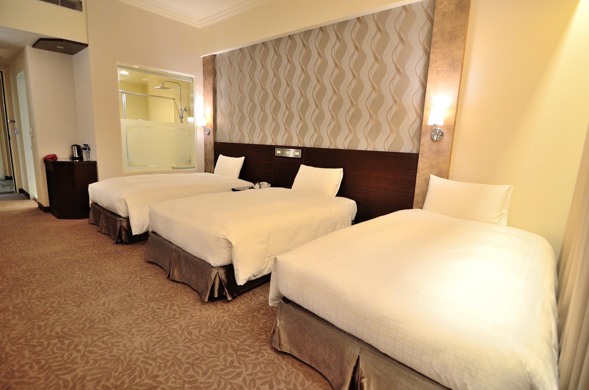 Royal Chiayi Hotel · 皇品國際酒店: A room with three single beds, headboard lights and a bathroom partition