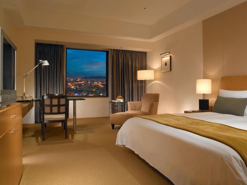 Ambassador Hotel Hsinchu: A room with a large bed, desk, armchair and a window overlooking the city