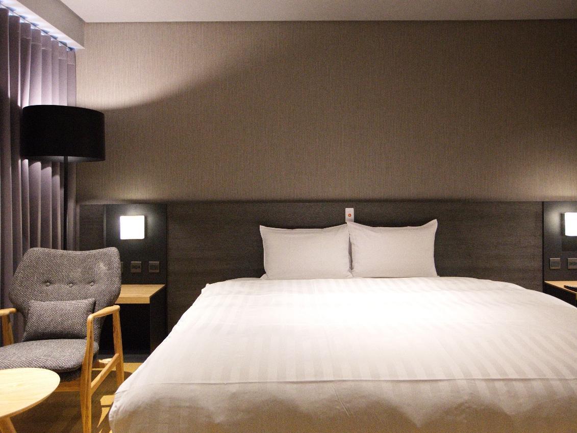 Chiayi Guanzhi Hotel: A bedroom with a large bed, padded headboard, curtains, armchair and round table