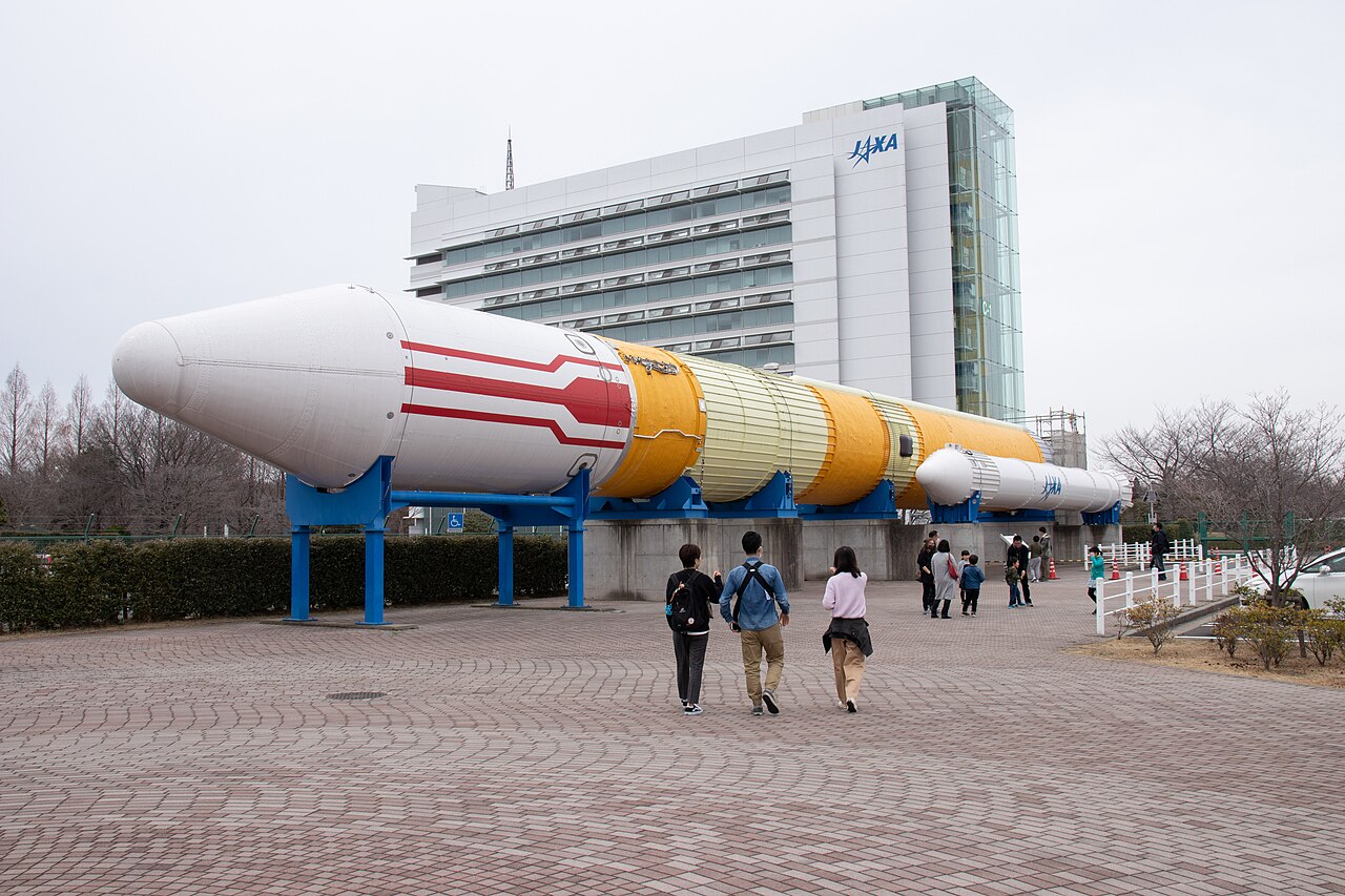 쓰쿠바 우주센터의 수평으로 전시된 H-II 로켓과 JAXA 건물, 2019년 사진